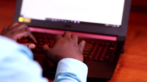 hombre escribiendo en una computadora mientras está sentado en un escritorio de madera