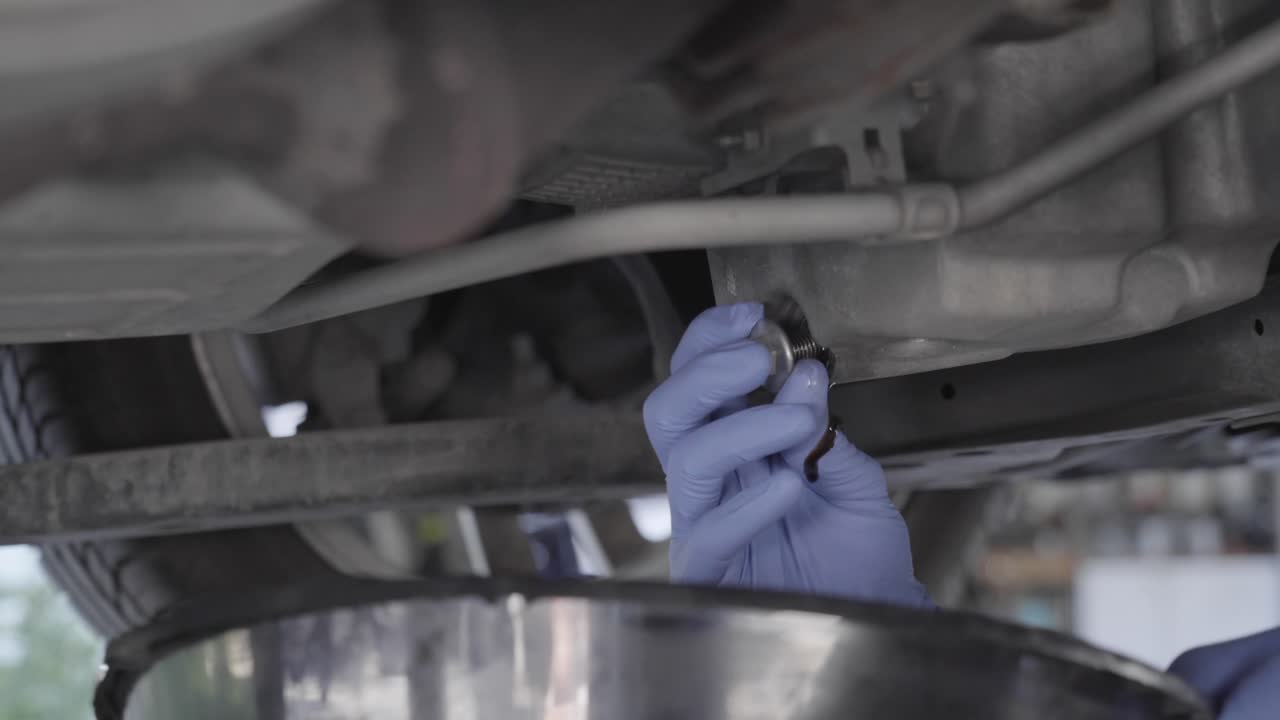 mecánico de automóviles drenando aceite de un automóvil durante un cambio de aceite