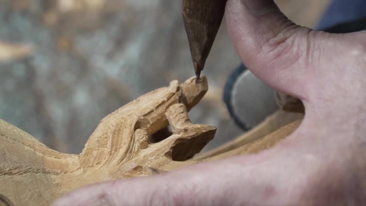 Craftsman carving a small sculpted figure on the surface of a wooden ink pot with a slender chisel