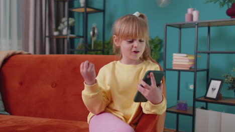 Girl-kid-enjoying-conversation-on-mobile-phone-with-friend-relaxing-sitting-on-couch-at-home-alone