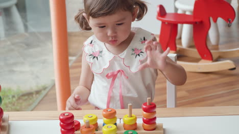 little girl 3-year-old stacking colorful rings on wooden columns in a wrong way - kid learning counting, sorting playing educational game promoting hand eye coordination, motor skills and creativity