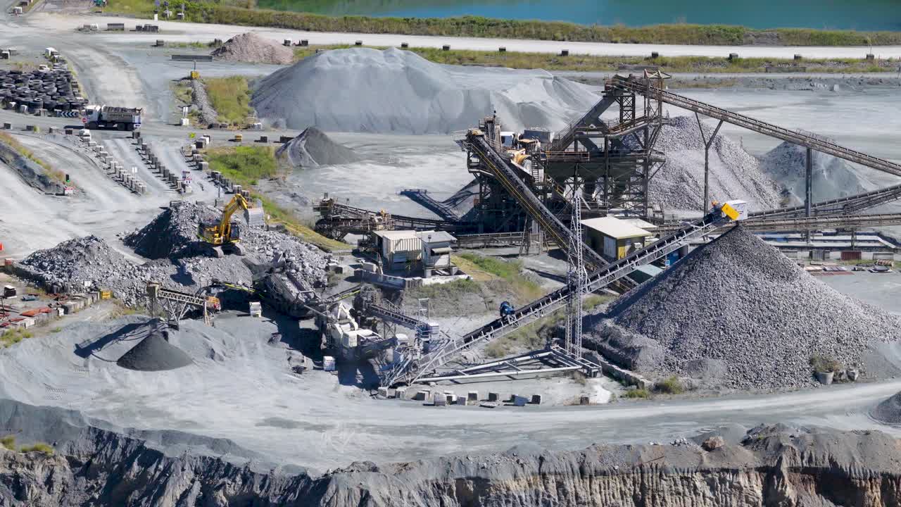 Drone footage captures active mining operations at a Gold Coast quarry, showcasing machinery, trucks, and excavators under bright daylight