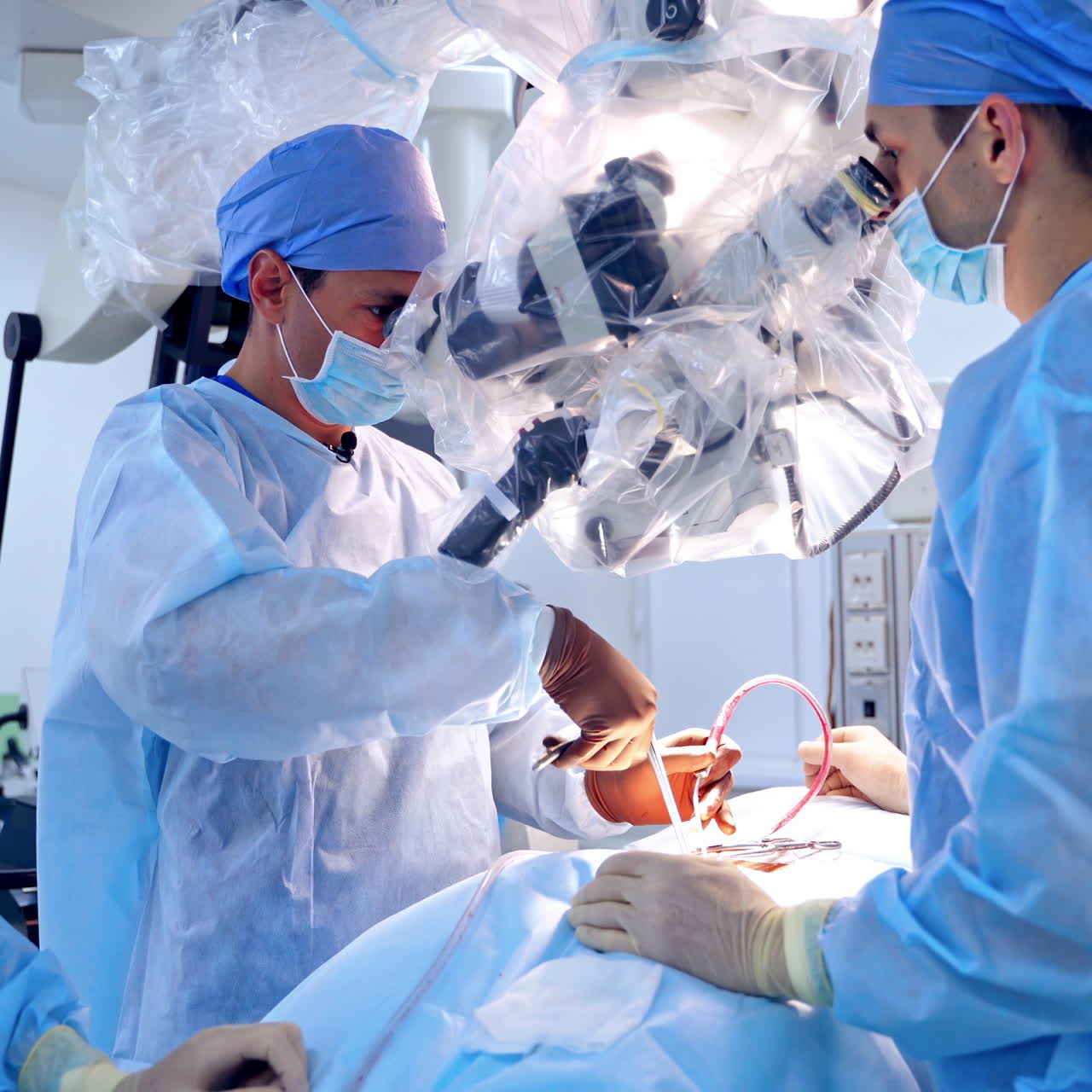 Group of surgeons performing operation to a patient. Doctors in medical uniform look into modern microscope during surgery in the operating room.