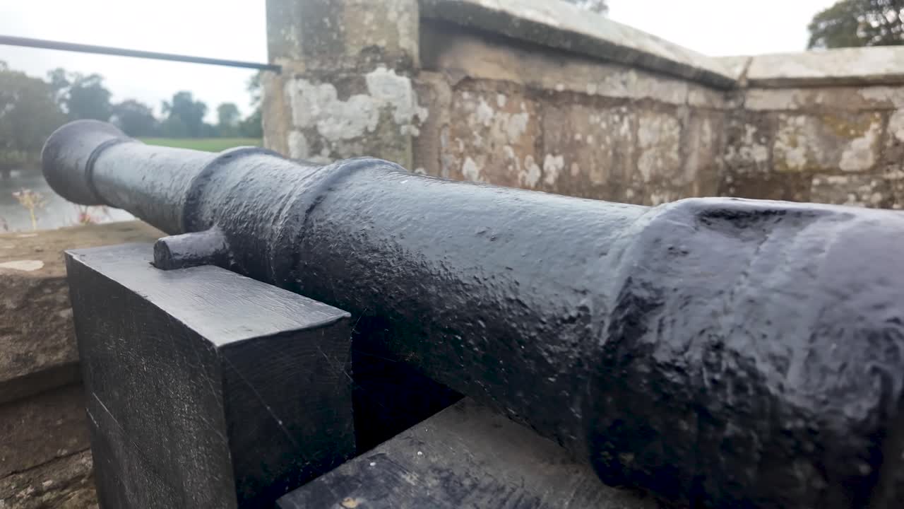Black cannon sitting on a wooden carriage next to a stone wall at a historic English castle