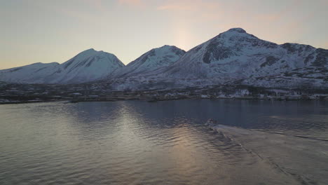 fishing boat sails toward town bellow mountain peaks