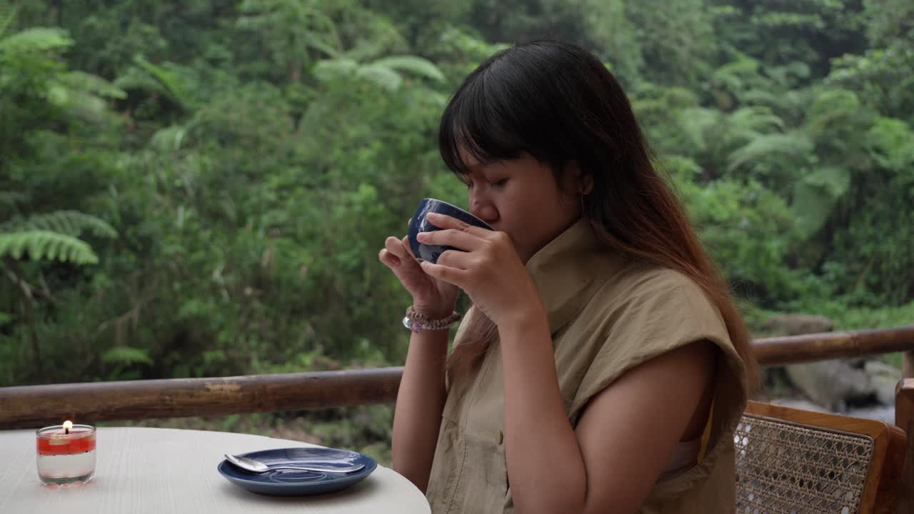 Indonesian girl enjoying tea on the balcony of a tropical eco-hotel