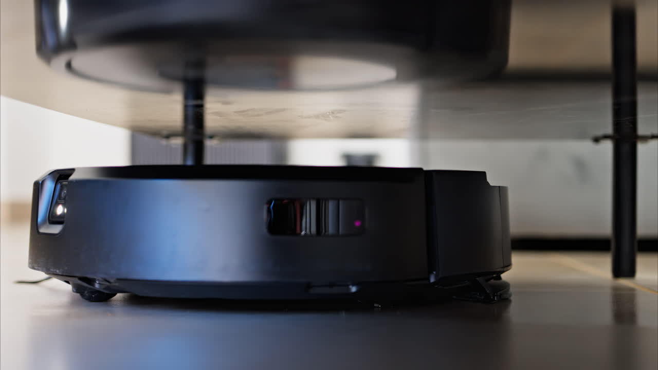 Close up of a small, black robot vacuum cleaning under surfaces in the house