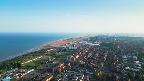 This-aerial-video-showcases-Skegness,-a-coastal-gem-in-Lincolnshire,-highlighting-its-long-sandy-beach,-bustling-tourist-district,-funfair-rides,-and-iconic-pier-on-a-summer-evening