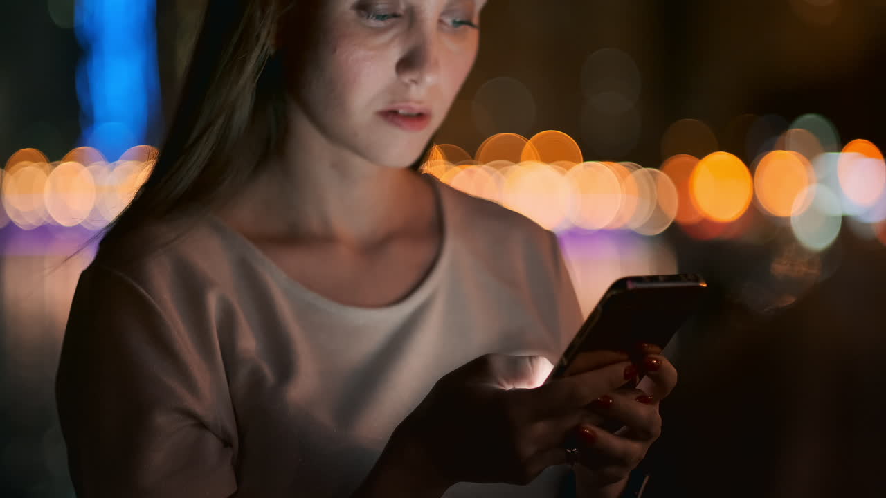 Young woman tourist travels through the night megalopolis and writes text messages on social networks about the journey holds the phone in her hands and looks at the screen of the gadget