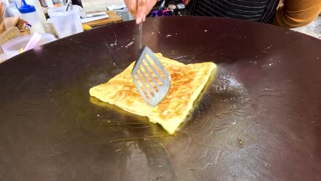 a street vendor expertly cooks fried roti on a hot griddle in kanchanaburi, thailand. the process highlights traditional techniques and vibrant street food culture