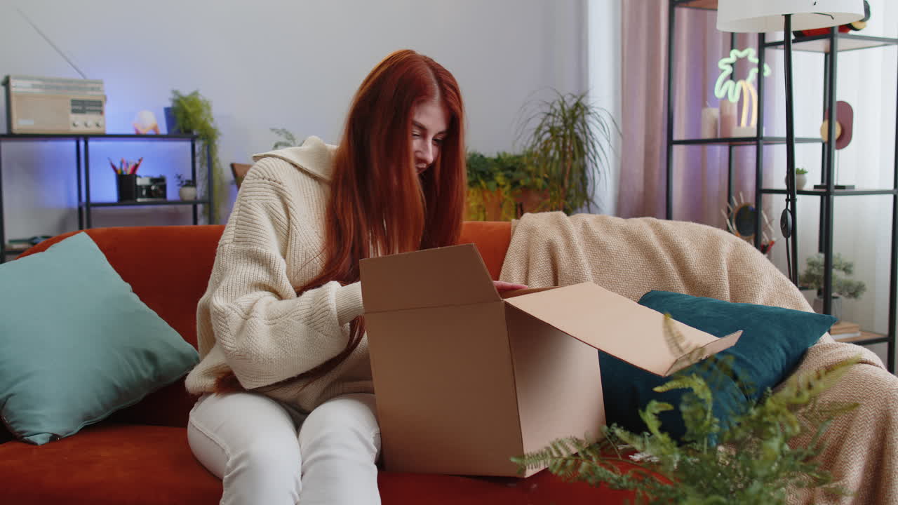 Happy young woman shopper unpacking cardboard box delivery parcel online shopping purchase at home