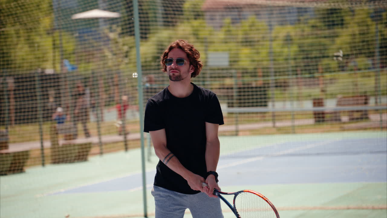 Man in black shirt playing tennis on a blue and green court on a sunny day