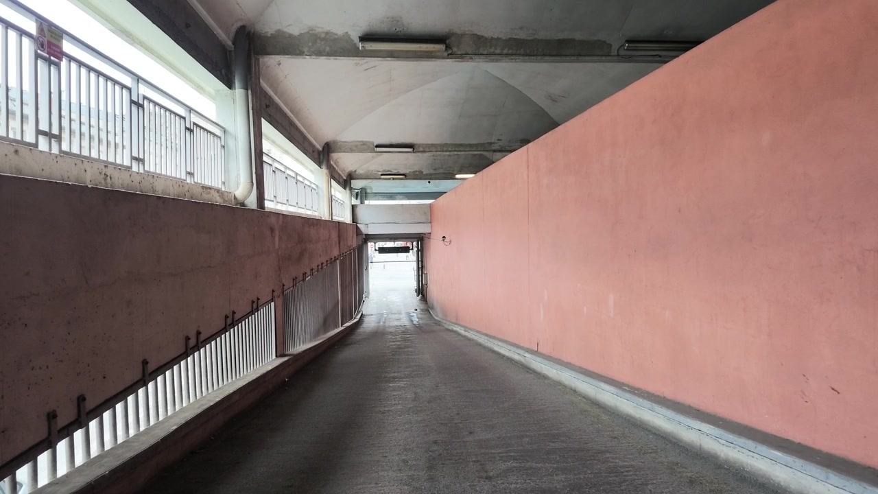 Un lento movimento di telecamera attraverso una rampa vuota di un parcheggio sotterraneo in cemento con pareti rosa.