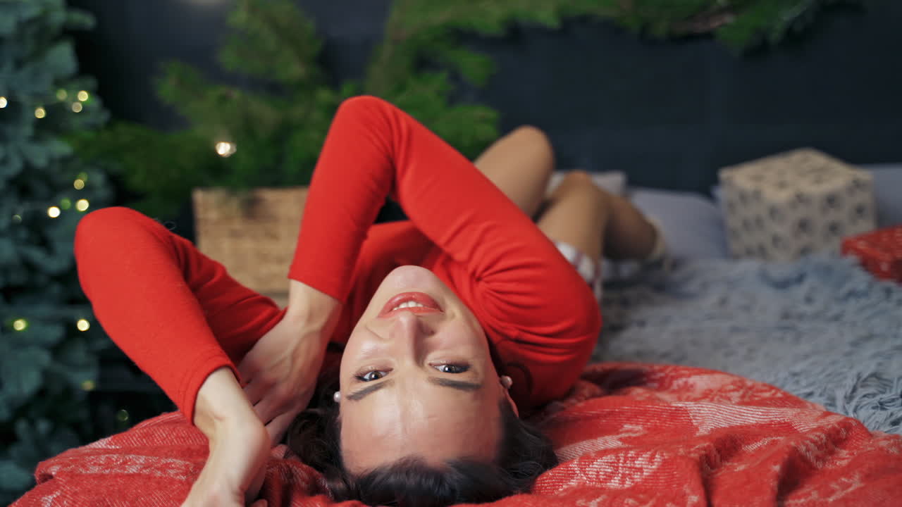 Very beautiful girl rolling in bed and posing to the camera. Room interior before winter holidays. Fest spirit.