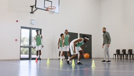 group of multiracial male basketball players avoiding cones and throwing basketball in gym