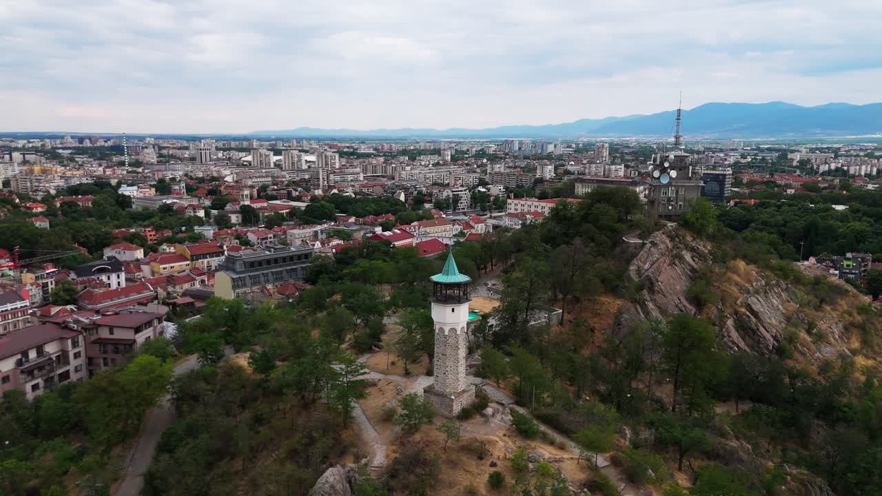 Um drone orbita a Torre do Relógio de Plovdiv no topo de Sahat Tepe e revela a cidade abaixo e as montanhas enevoadas que se estendem ao longe.