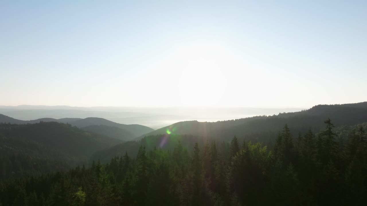 Sunrise over forested mountains with light mist and clear blue sky