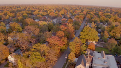 aerial push over beautiful neighborhood in kirkwood, missouri in autumn at golden hour past a small church and over houses and trees