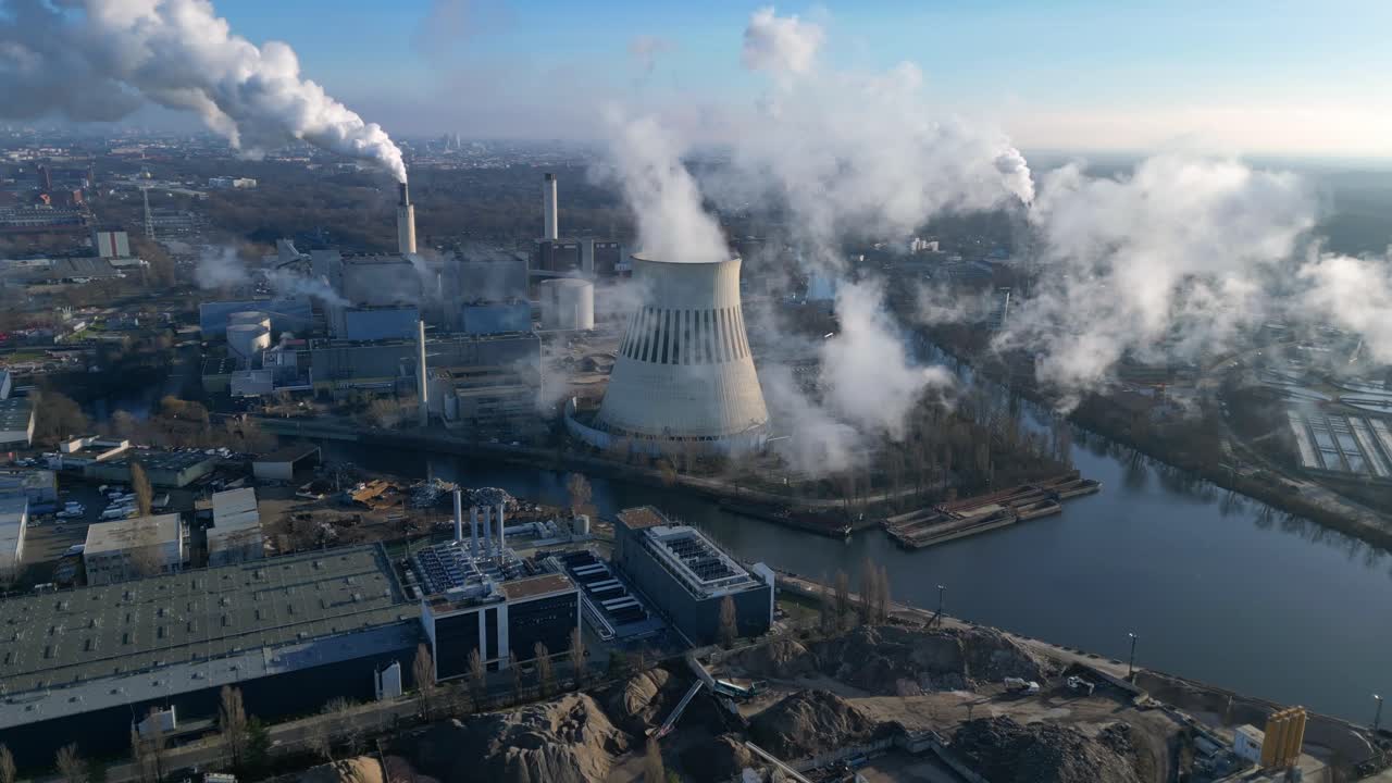 power plant emitting steam from its cooling tower, situated by a river and overlooking the cityscape. Best aerial view flight panorama orbit drone