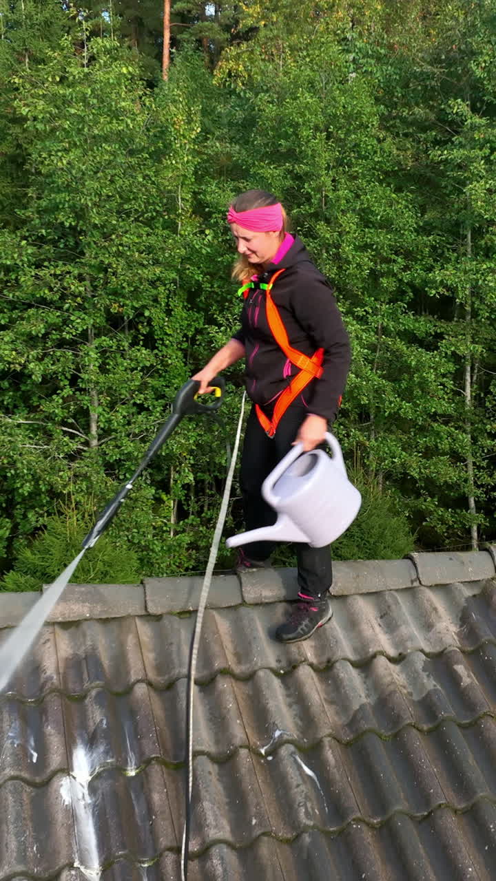 Vertical drone shot of a woman cleaning a rooftop of a house, sunny day