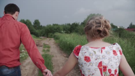 couple walking hand-in-hand in a countryside path on a cloudy day
