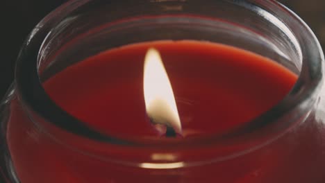 shimmering flame of lit red candle in a glass holder