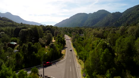 Drone view of a car driving along a forested road near the Petrohué River in southern Chile. Surrounded by lush greenery and mountains, the scene captures peaceful rural travel
