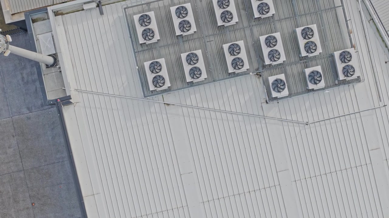 Aerial footage of a modern data center rooftop with multiple HVAC systems. Clean industrial lines, metallic textures and high-angle drone shot highlight advanced cooling infrastructure in daylight.