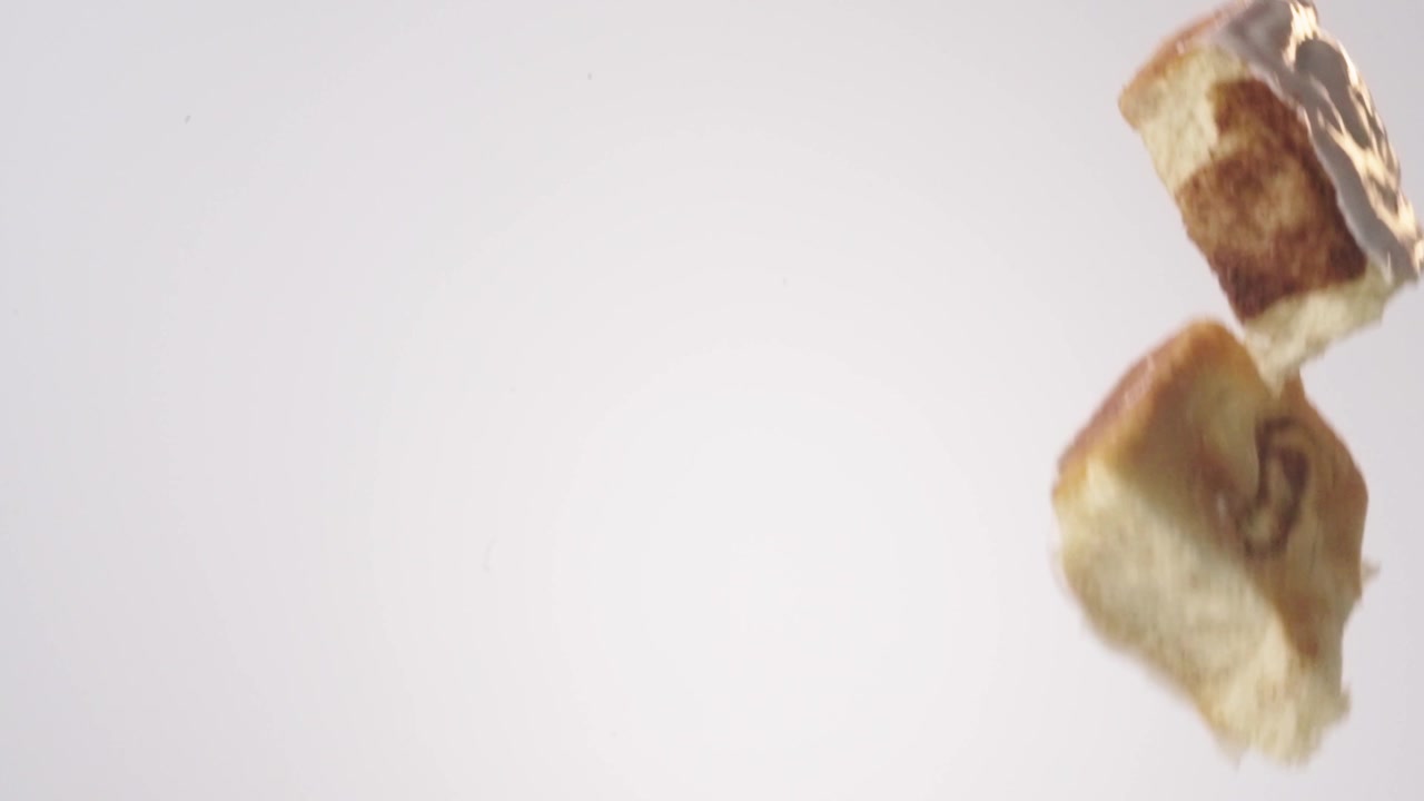 Girelle alla cannella glassate che cadono su uno sfondo bianco senza soluzione di continuità in slow motion cinematografico. Contenuti per la mattina delle feste, reel per il brunch di Natale, post per la colazione della domenica.