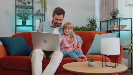 Child-kid-daughter-having-fun-with-father-or-nanny-enjoying-using-laptop-pc-make-video-call-at-home