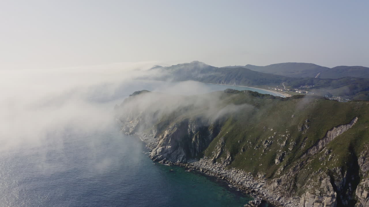 Vista a volo d'uccello di una costa rocciosa epica e mozzafiato con nebbia fitta e densa che si avvicina dal mare, Estremo Oriente, Russia