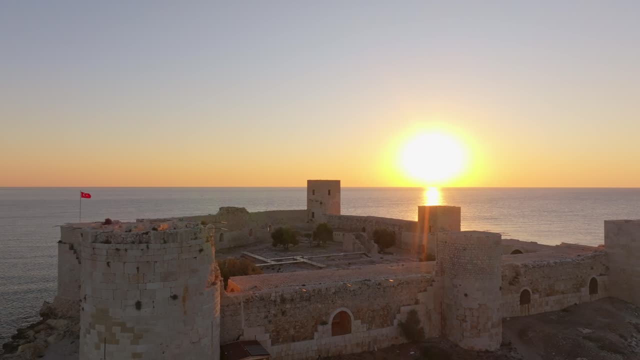 Castelo medieval resplandecendo no nascer do sol dourado sobre o Mediterrâneo calmo.