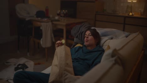 woman relaxing on couch, eating chips at home