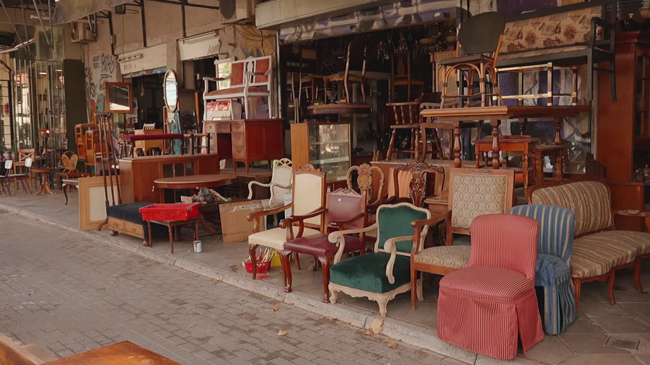 Tienda de antigüedades con sillas y muebles vintage en una calle soleada.
