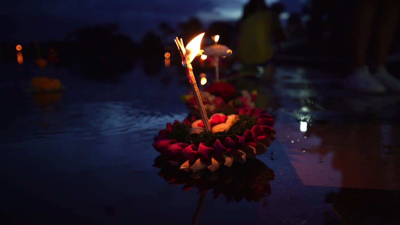 festival loy krathong: colorido krathong inclinado a la izquierda, flotando en el agua azul oscuro del lago con una vela encendida y una instancia en la parte superior