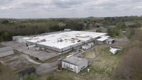 aerial drone footage moving towards an abandoned, decaying factory, with a truck depot and train line