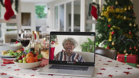 feliz mujer mayor afroamericana en computadora portátil acostada en la mesa de navidad