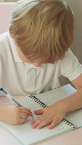 little blond pupil draws spot with pen and wipes by finger in notebook in home classroom. toddler boy does creative work in copybook in kindergarten