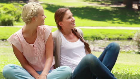 Woman-sitting-as-her-friend-sits-down-with-her-as-they-then-talk-and-look-to-the-side