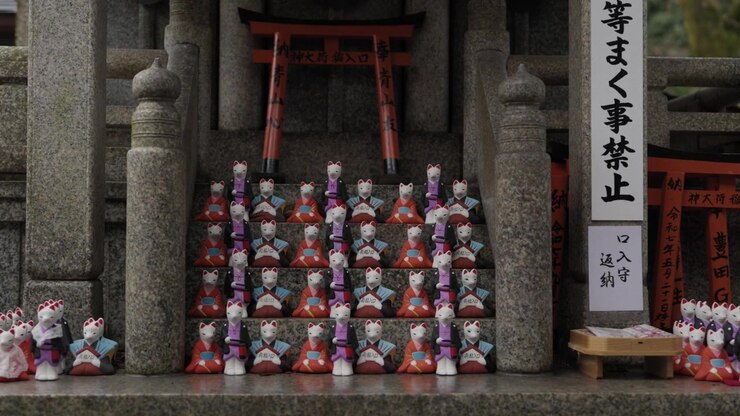 Statuette di volpi Kitsune allineate sui gradini di pietra al Santuario Fushimi Inari a Kyoto, Giappone.