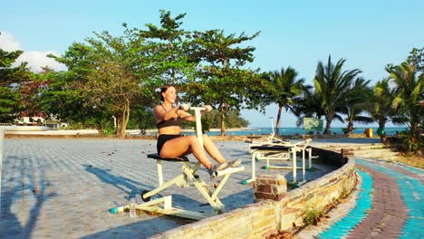 chica con traje deportivo haciendo ejercicio en bicicleta en el gimnasio al aire libre del jardín del resort de vacaciones con árboles tropicales en indonesia
