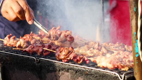 person cooking skewered meat on a charcoal grill