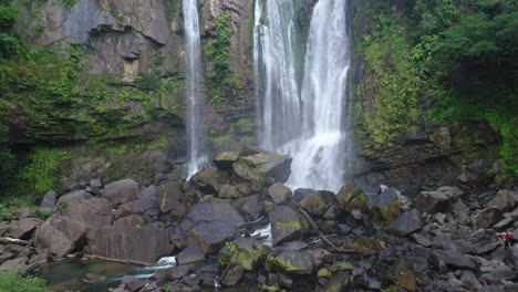 Aéreo-De-Las-Cascadas-De-Nauyaca-Con-Un-Hombre-Caminando-En-La-Base-De-La-Selva-Tropical,-4k