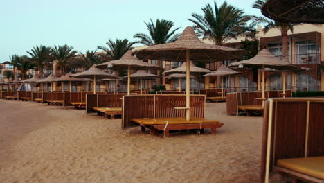 Cane-umbrellas-and-sunbeds-on-sunset-beach.-Resort-parasols-on-sky-background.