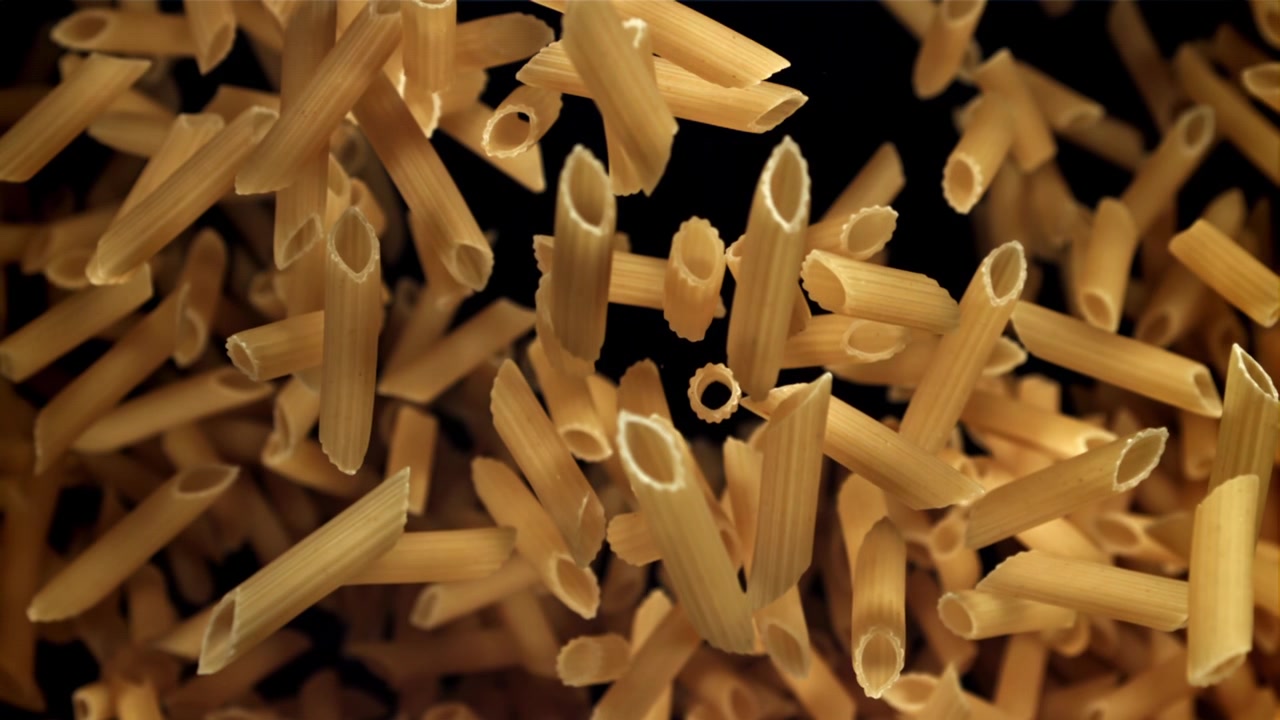 Penne secche che cadono al rallentatore su sfondo nero