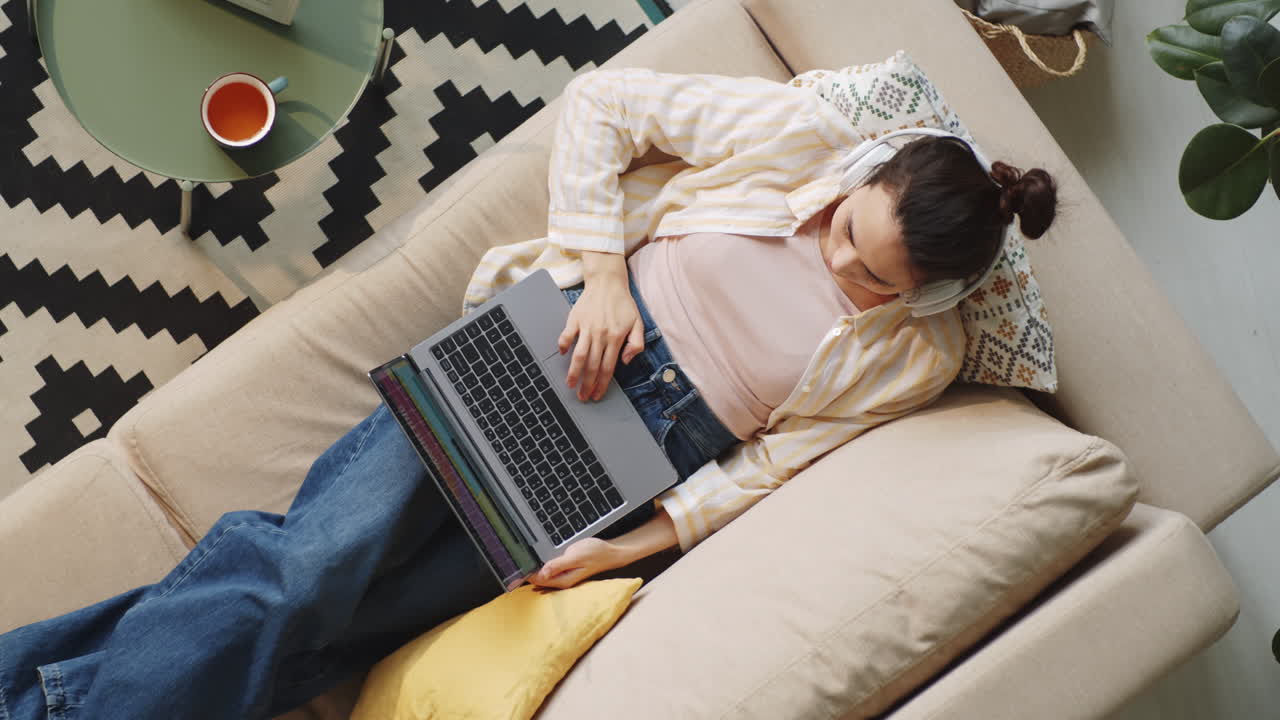 Woman in Headphones Using Laptop on Sofa