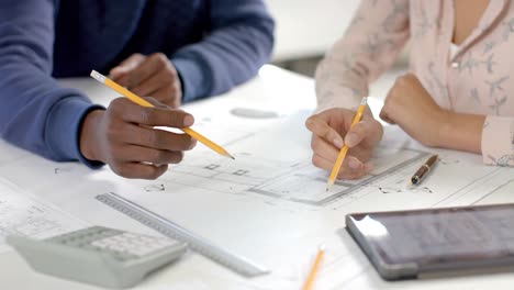 Diverse-architect-colleagues-discussing-work-at-table-with-blueprint-and-tablet-in-slow-motion