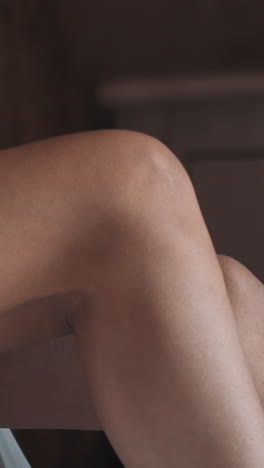 young woman wraps up bare legs with elegant white dressing gown sitting on bed in hotel room close view. attractive lady in stylish luxury lingerie