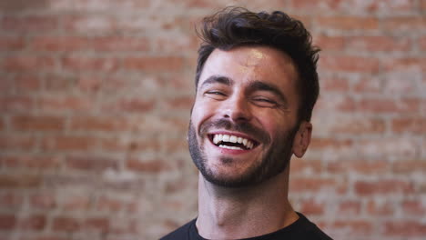 Head-And-Shoulders-Portrait-Of-Smiling-Hispanic-Man-Standing-Against-Brick-Wall-In-Coffee-Shop