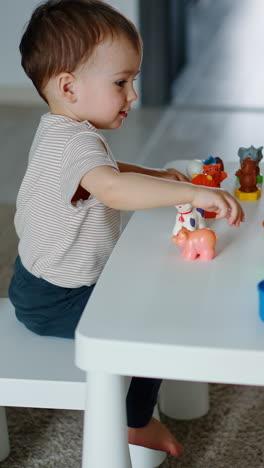 adorable baby plays with toys at the table. kid pushes the cup and watches it roll. vertical video
